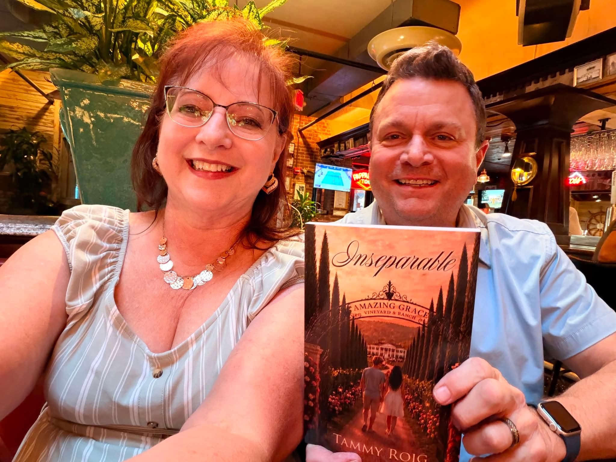 Tammy Roig smiling and holding a physical copy of Inseparable together with a companion at a celebratory gathering.